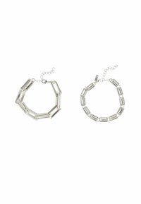 Deux bracelets en argent : à gauche, une chaîne angulaire avec des maillons allongés ; à droite, des maillons rectangulaires avec des connecteurs, tous deux terminés par des fermoirs réglables.