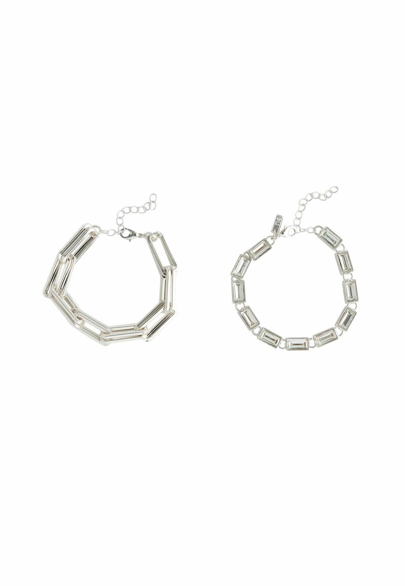 Deux bracelets en argent : à gauche, une chaîne angulaire avec des maillons allongés ; à droite, des maillons rectangulaires avec des connecteurs, tous deux terminés par des fermoirs réglables.