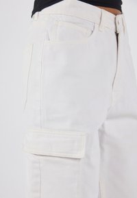 Hvite cargo-bukser laget av denim, med en sidelommen, klassisk fem-lomme design og synlige sømmer langs sømmene.
