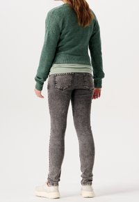 Grön stickad tröja med ribbat mönster, tillsammans med ljusgrå tajta jeans med en urtvättad look och bakfickor. Vita sneakers fulländar stilen.