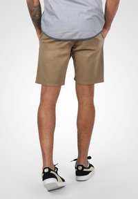 Pantalones cortos caqui hechos de una mezcla de algodón con una textura suave, con un corte recto y detalles de costura sutiles, combinados con zapatillas negras y beiges.