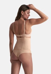Shapewear beige con spalline regolabili e chiusura posteriore a gancio e occhiello. Il tessuto è liscio ed elasticizzato, offrendo supporto e modellatura.