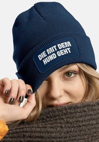 Navy knitted beanie with a textured surface, featuring a rectangular patch with white text reading "DIE MIT DEM HUND GEHT."