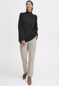 Pulover negru cu guler înalt și mâneci largi, asortat cu pantaloni bej cu carouri și botine maro cu toc. Material simplu, texturat.