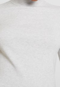 Ljusgrått polotröja gjort av ribbat tyg. Har en nära sittande halsringning och en mjuk textur, lämplig för lager-på-lager.