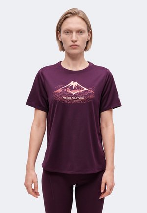 Vrouw draagt een paars T-shirt met korte mouwen met een gestileerde berg en de tekst "ASICS FUJITRAIL" op de voorkant, staand tegen een effen achtergrond.
