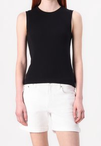 Svart ärmlös topp i åtsittande ribbat material, kombinerad med uppvikta vita denimshorts, som framhäver en jämn textur och klassisk design.