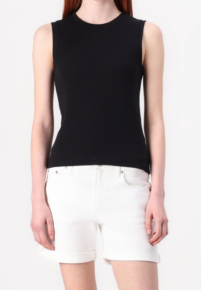 Svart ärmlös topp i åtsittande ribbat material, kombinerad med uppvikta vita denimshorts, som framhäver en jämn textur och klassisk design.