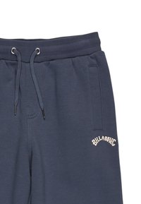 Tamno plave trenirke od teksturiranog materijala, s elastičnim pojasom, zatvaranjem na vezicu, bočnim džepovima i bijelim izvezenim logom branda.