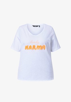 Biała, krótka koszulka z dekoltem w serek z nadrukiem "lovely KARMA", gdzie "lovely" jest napisane jasnym pismem a "KARMA" teksturowanymi pomarańczowymi literami.