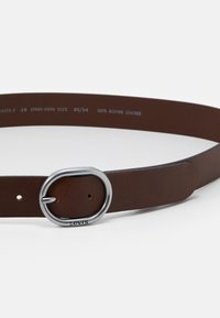 Ceinture en cuir bovin marron avec une boucle en métal argenté en forme de cercle. Présente des informations de taille imprimées sur le côté intérieur. Texture plate et lisse.