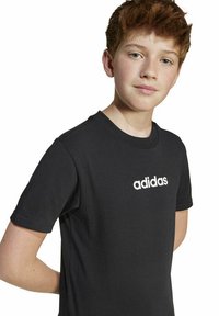 Melnas īsām piedurknēm kokvilnas T-kreklas ar baltu Adidas logotipu uz krūtīm. Vienkāršs dizains ar apaļu kaklu un standarta piegriezumu.