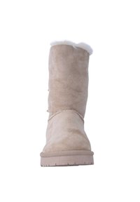 Beżowe zamszowe botki do połowy łydki z białym futrzanym wykończeniem na górze, z teksturowaną podeszwą oraz dekoracyjnym łańcuchem na środkowej części.