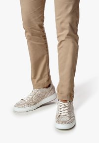 Sneakers bianchi a trama con un design a motivi, dotati di lacci crema e una suola bianca, abbinati a pantaloni beige chiaro.