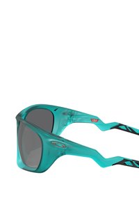 Occhiali da sole color acquamarina con montatura trasparente, lenti grigie, design angolare e bracci texturizzati con accenti neri e logo.