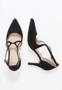 Eleganti scarpe con tacco alto in suede nero, con punta affusolata e design a T-strap. Presentano un tacco sottile e un lato aperto per la ventilazione.