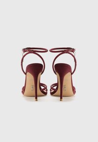 Burgundy high-heeled sandals with glittering ankle straps, a smooth suede finish, and slender stiletto heels. Open back design.
