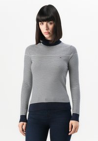 Suéter a rayas en gris y azul marino, con un cuello alto y puños acanalados. Fabricado en un tejido suave con un diseño ajustado.