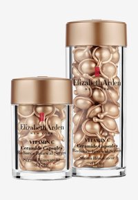 Två transparenta behållare med guldiga lock, fyllda med gyllene ceramidkapslar. Etiketterna visar "Vitamin C" och produktinformation i svart text.