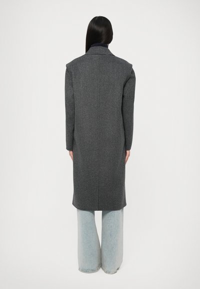 Cappotto di lana grigio con maniche lunghe e colletto alto, caratterizzato da un design strutturato e una vestibilità dritta, abbinato a pantaloni larghi in denim chiaro.