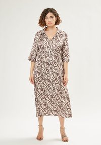 Langes, knöpften Kleid in braunen und cremigen Wirbelmustern. Leichter Stoff mit Kragen und Dreiviertelärmeln. Glatte Textur.