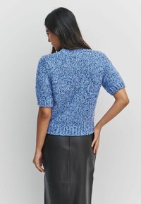 Short-sleeve knitted sweater in light blue with a textured, loose fit and ribbed hem, paired with a black sleek leather skirt.