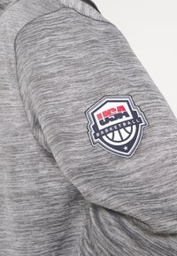 Grauer Heather-Sweatshirt mit Stoffstruktur und einem USA Basketball-Logo-Patch in Rot, Weiß und Blau am linken Ärmelsaum.