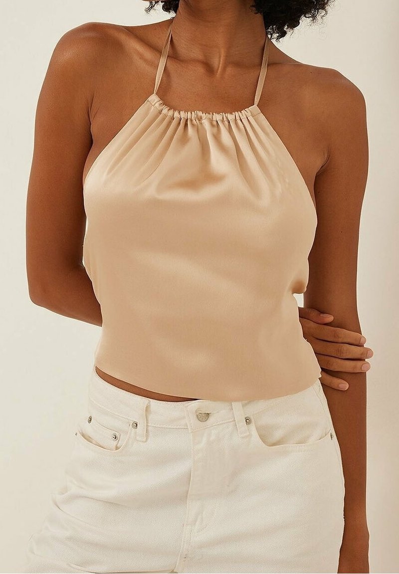 Haut à col bénitier en satin beige avec un col froncé et des bretelles fines, associé à un short en denim blanc taille haute. Texture lisse.