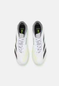 Baskets de football blanches avec des rayures noires et des accents jaunes vifs. Tige texturée avec de petites perforations et un design à lacets.