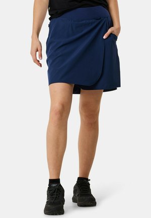 Granatowa spódnica szorty wykonana z lekkiego materiału, z designem w formie owijania, z boczną kieszenią, w połączeniu z czarnymi butami sportowymi.