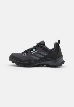 Schwarzer und dunkelgrauer Adidas Terrex Trailrunning-Schuh mit robuster Sohle, Mesh-Obermaterial und hellblauen Schnürsenkelösen, Seitenansicht vor weißem Hintergrund.