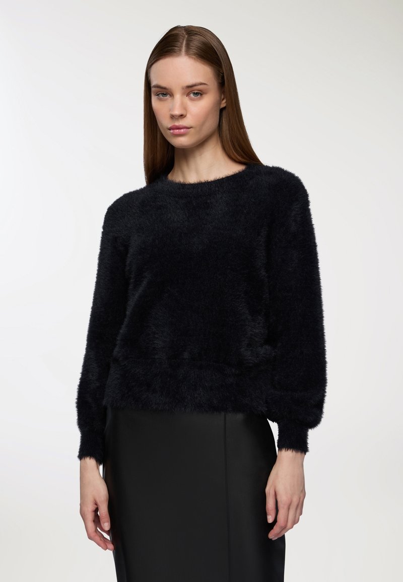 Czarny puszysty sweter z okrągłym dekoltem i długimi rękawami. Materiał wygląda na miękki i teksturowany, zestawiony z gładką czarną spódnicą.