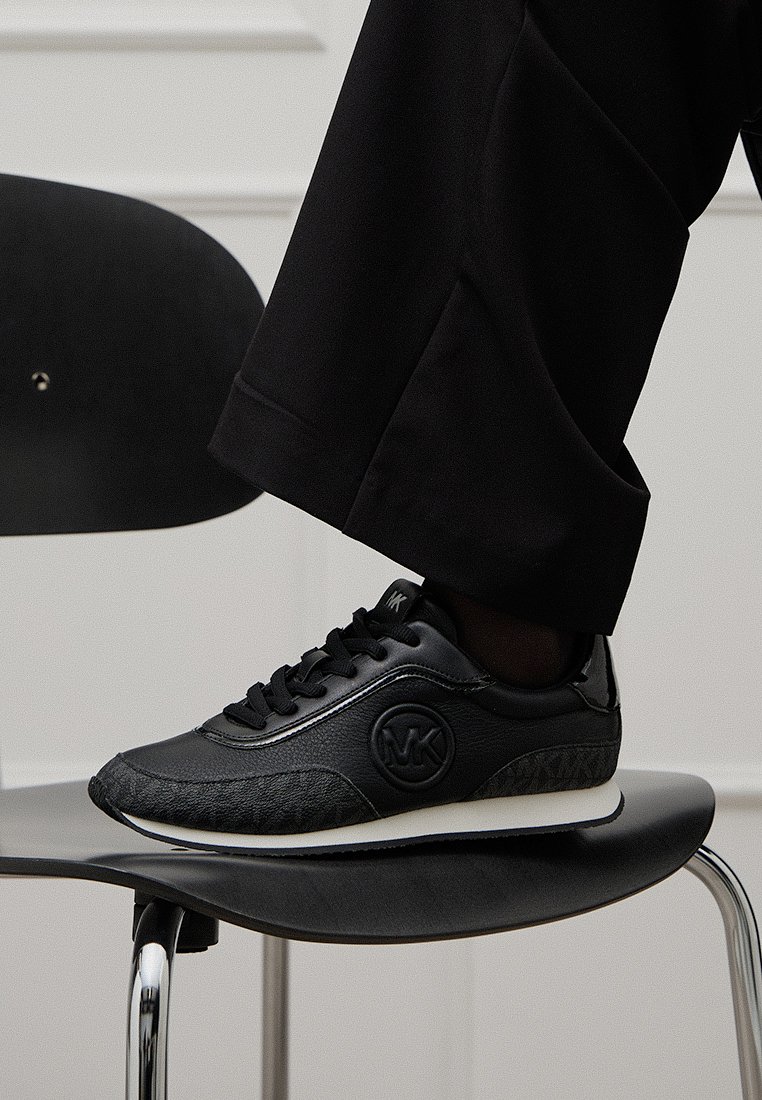 Zwarte sneakers met een leren bovenkant, met een textuur aan de zijkant, logo embellissement, vetersluiting en een witte rubberen zool.