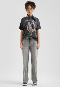 Zwarte grafische T-shirt met een Metallica ontwerp, gecombineerd met lichtgrijze high-waisted jeans en zwart-witte sneakers. Gelaagde sjaal om de nek.