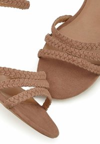 Bruine suède sandalen met gevlochten banden en een puntige neus. Heeft een soepele binnenzool en een platte, lichtbruine buitenzool.