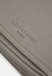 Szary skórzany portfel z teksturowaną powierzchnią, wytłoczonym logo marki i starannym przeszyciem wzdłuż krawędzi. Smukły, składany design.