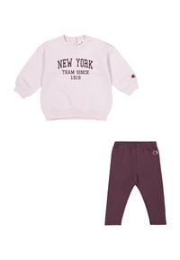 Sudadera rosa clara con el texto "NEW YORK TEAM SINCE 1919", combinada con leggings morados oscuros que presentan un parche con el logo. Tejido suave, ajuste relajado.