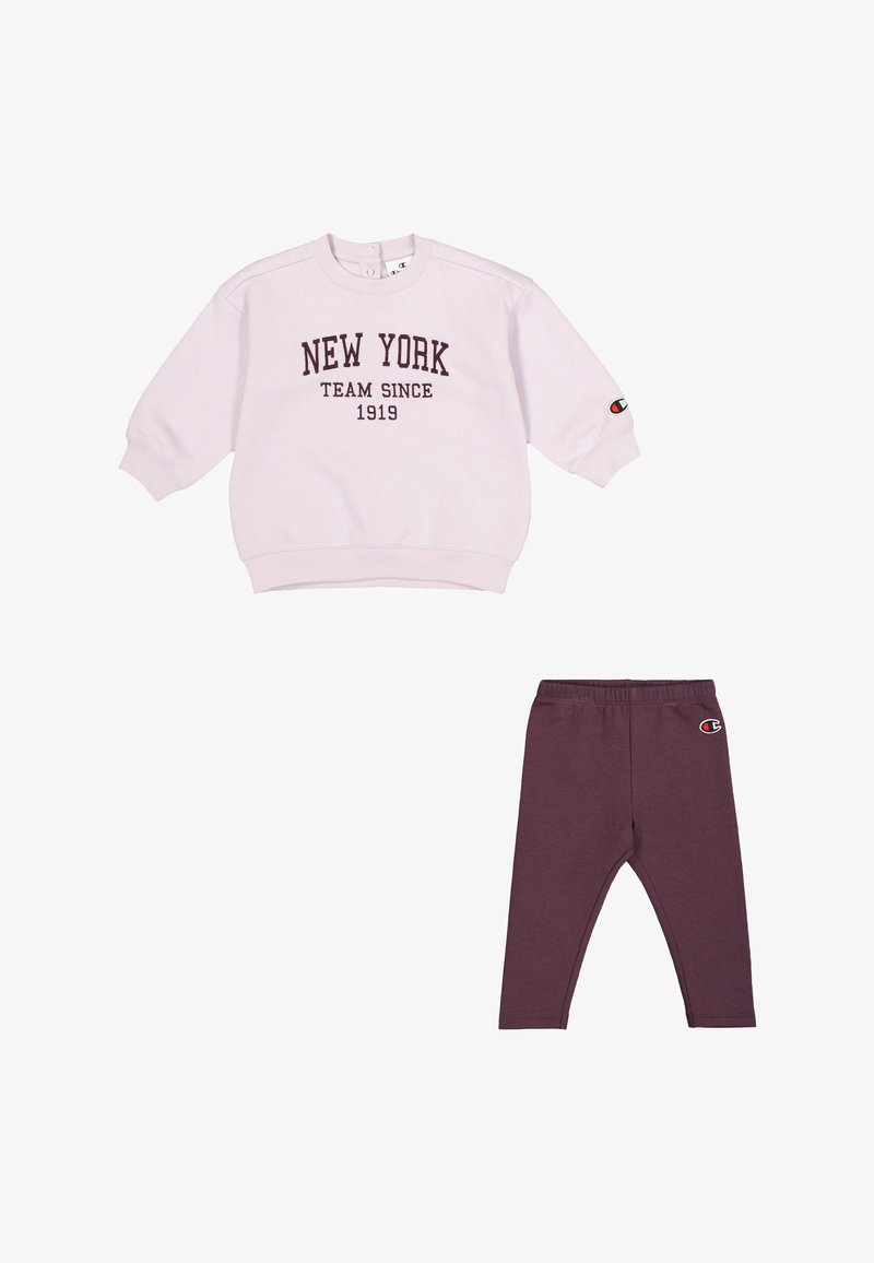Felpa rosa chiaro con la scritta "NEW YORK TEAM SINCE 1919", abbinata a leggings viola scuro con un patch del logo. Tessuto morbido, vestibilità rilassata.