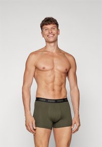 Zöld pamut boxer alsónemű fekete gumis derékkal, amelyen a "PUMA" logó található, egy mezítelen felsőtestű férfi modell bemutatásában.