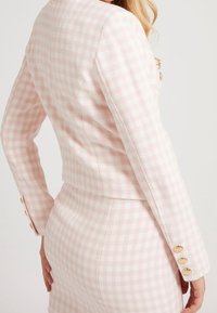 Rosa kariertes Blazer mit tailliertem Schnitt, ausgestattet mit goldfarbenen Knöpfen und einem strukturierten Stoff. Die Rückansicht zeigt die maßgeschneiderte Silhouette.