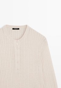 Pull henley en tricot rose clair avec un motif texturé, doté d'un col rond et de quatre boutons sur le devant. Détails comprenant des bords côtelés.