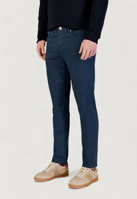 Pantaloni aderenti color blu navy realizzati in tessuto misto cotone, con tradizionale design a cinque tasche e texture liscia, abbinati a scarpe da ginnastica beige.