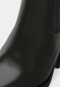 Must musta ankle boot, mille musta läike, külgmised elastsed paneelid ja madal virnastatud konts.