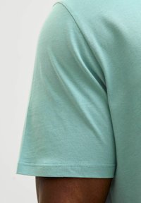 Miętowa bawełniana koszulka z okrągłym dekoltem i krótkimi rękawami, o gładkiej fakturze i standardowym wykończeniu na dole.