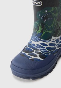 Botte de pluie en caoutchouc bleue avec une semelle texturée, un design graphique d'une créature verte et des vagues aux tons blancs et bleus, avec une finition lisse.