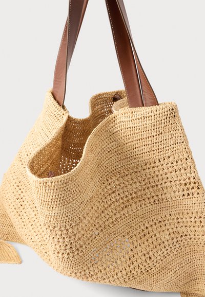 Μπεζ πλεκτή τσάντα ώμου με φαρδιές καφέ δερμάτινες λαβές, ανοιχτό πάνω μέρος και υφασμένο μοτίβο κροσέ.