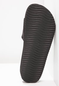 Black rubber sandal sole featuring a textured surface with horizontal grooves for traction. The design is flat and minimalistic.