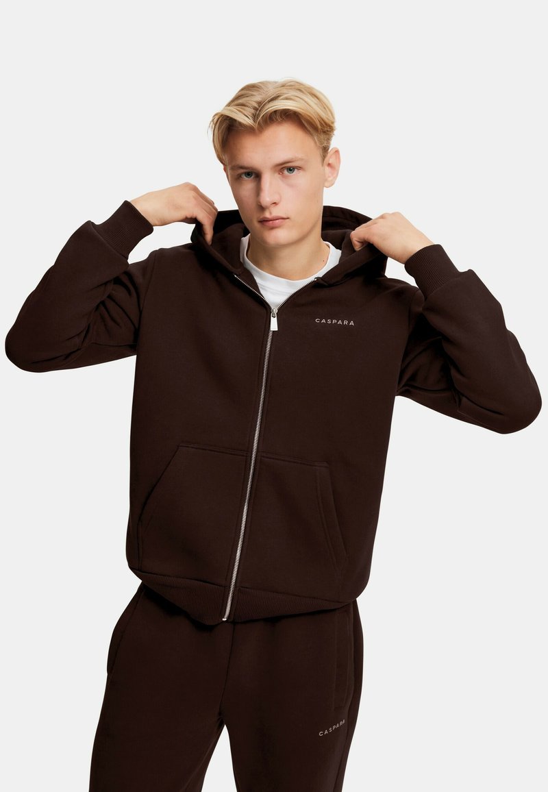 Mørkebrun zip-up hettegenser laget av mykt stoff, med en front lommesekk, ribbede mansjetter og hette. Liten logo på brystet.