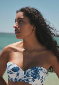 Top bikini bandeau con base bianca e motivo floreale blu. Tessuto morbido, design aderente, con un leggero arriccio al centro.