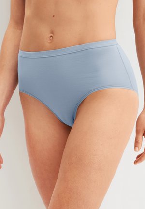 Femme portant un sous-vêtement sans couture taille haute bleu clair, montrée de la moitié du torse à la moitié des cuisses sur un fond uni.